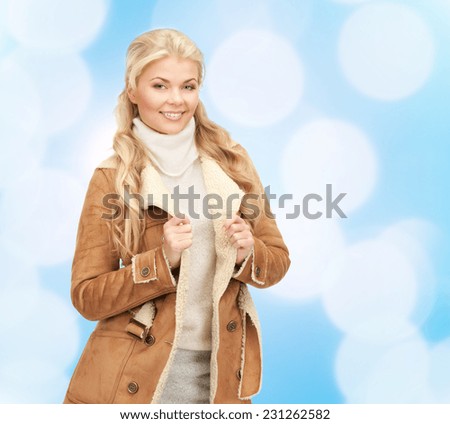 winter holidays, christmas, fashion and people concept - smiling young woman in winter clothes over blue lights background