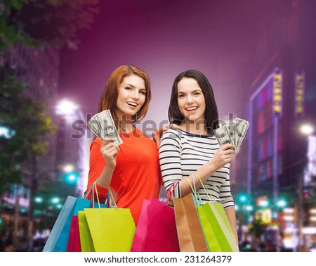 sale, friendship and people concept - two smiling teenage girls with shopping bags and cash money over night city background