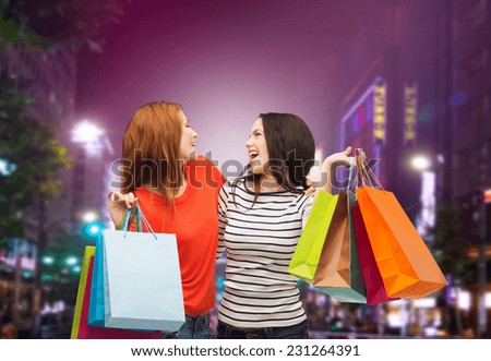 sale, friendship and people concept - two smiling teenage girls with shopping bags over night city background