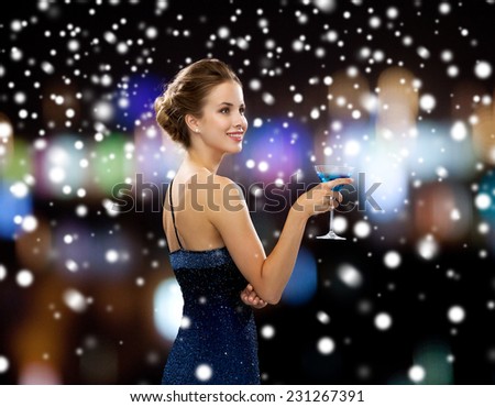party, drinks, holidays, people and christmas concept - smiling woman in evening dress holding cocktail over night lights and snow background