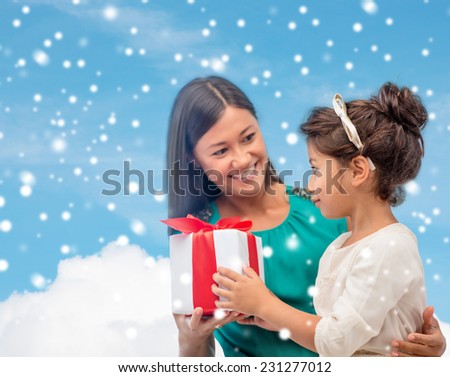 christmas, holidays, family and people concept - happy mother and child girl with gift box over blue snowy sky with cloud background