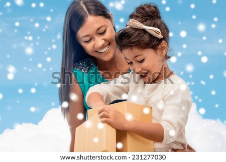 christmas, holidays, family and people concept - happy mother and child girl with gift box over blue snowy sky with cloud background