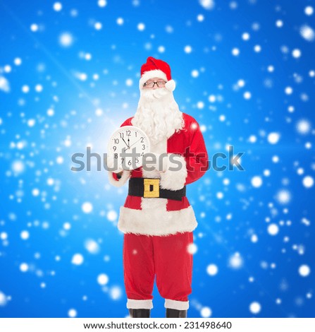 christmas, holidays and people concept - man in costume of santa claus with clock showing twelve over blue snowy background
