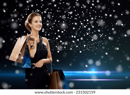 people, shopping, sale, christmas and holidays concept - smiling woman in dress with shopping bags over night lights and snow background