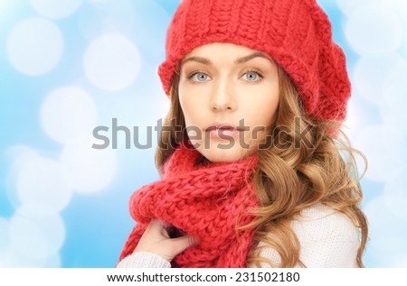 happiness, winter holidays, christmas and people concept - close up of young woman in red hat and scarf over blue lights background