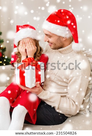 christmas, holidays, family and people concept - smiling father and daughter in santa hats holding gift box and covering eyes at home