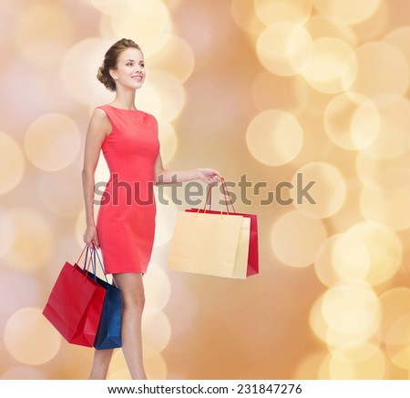 shopping, sale, christmas and holidays concept - smiling elegant woman in red dress with shopping bags over beige lights background
