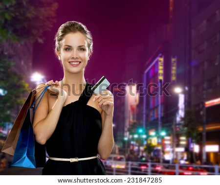 people, sale, christmas and holidays concept - smiling elegant woman in evening dress with shopping bags and credit card over night city background