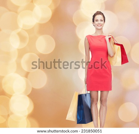 shopping, sale, christmas and holidays concept - smiling elegant woman in red dress with shopping bags over beige lights background