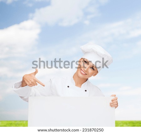 cooking, advertisement and people concept - smiling female chef, cook or baker pointing finger to white blank board over blue sky and grass background