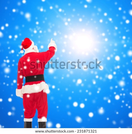 christmas, holidays and people concept - man in costume of santa claus pointing finger from back over blue snowy background