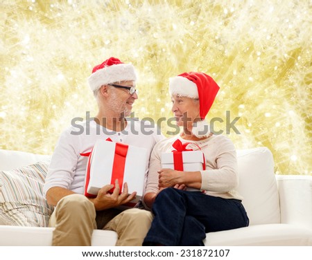 family, holidays, christmas, age and people concept - happy senior couple in santa helper hats with gift boxes over yellow background