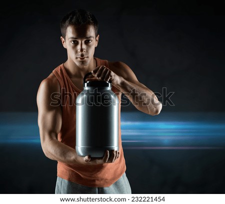 sport, bodybuilding, strength and people concept - young man standing holding jar with protein over dark background