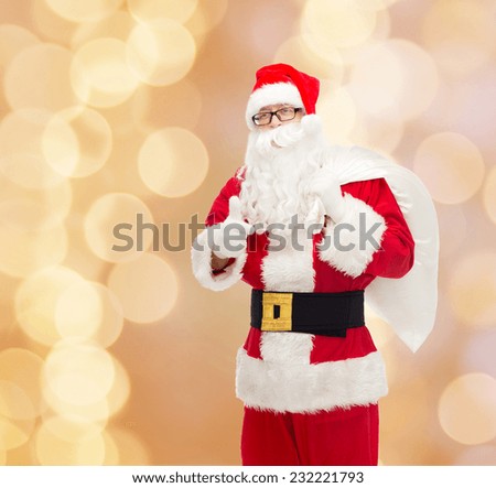 christmas, holidays, gesture and people concept - man in costume of santa claus with bag showing thumbs up over beige lights background