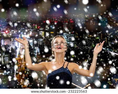 people, happiness, holidays and christmas concept - smiling woman raising hands and looking up over snowy night city background
