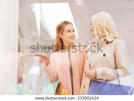 sale, consumerism and people concept - happy young women with shopping bags pointing finger to window in mall
