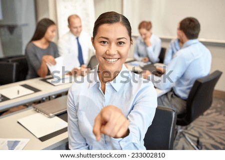 business, people and teamwork concept - smiling businesswoman pointing finger up with group of businesspeople meeting in office