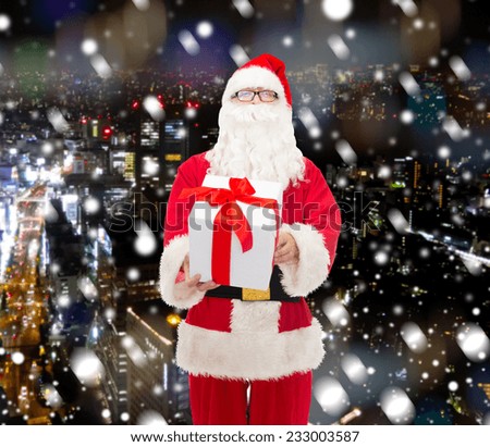 christmas, holidays and people concept - man in costume of santa claus with gift box over snowy night city background