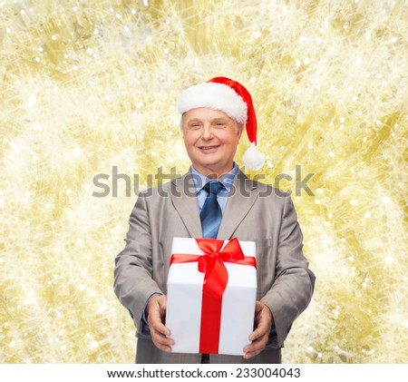 business, christmas, presents and people concept - smiling senior man in suit and santa helper hat with gift over yellow lights background