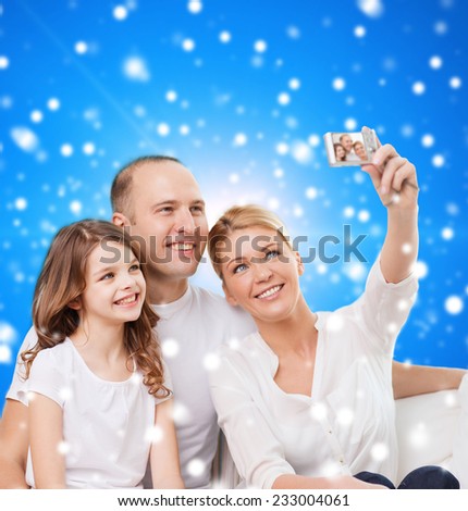 family, holidays, christmas, technology and people - smiling family  making selfie with camera over blue snowy background