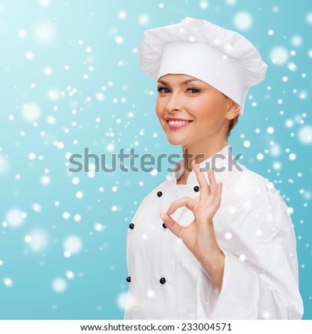 christmas, cooking, profession, gesture and people concept - smiling female chef showing ok hand sign over blue snowy background