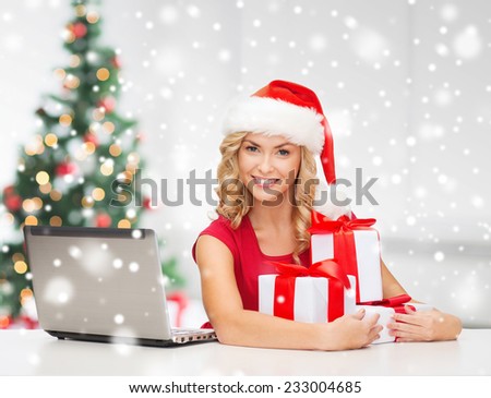 technology, holidays, online shopping and people concept - woman in santa helper hat with gift boxes and laptop computer over living room background