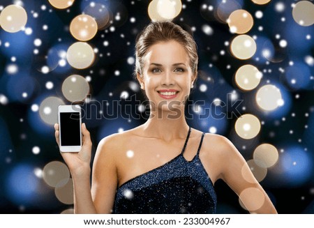 technology, christmas, holidays, advertising and people concept - smiling woman in evening dress holding smartphone over night lights and snow background