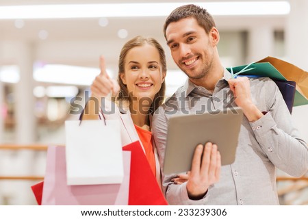 sale, consumerism, technology and people concept - happy young couple with shopping bags and tablet pc computer pointing finger in mall