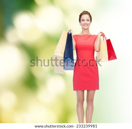 shopping, sale and holidays concept - smiling elegant woman in red dress with shopping bags over green background
