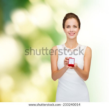 wedding, love, engagement and people concept - smiling woman in white dress holding red gift box with diamond ring over green background