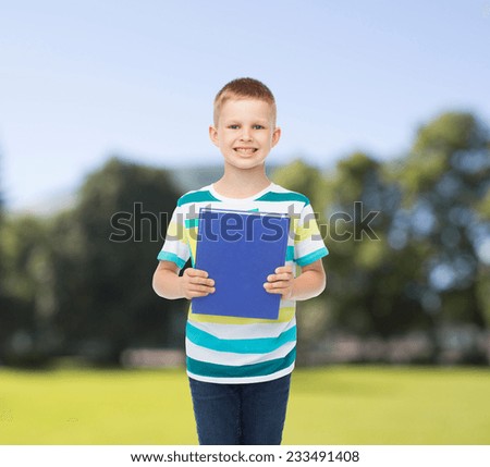 education, childhood and school concept - smiling little student boy with blue book over park background