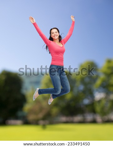 happiness, freedom, summer, nature and people concept - smiling young woman jumping in air over park background