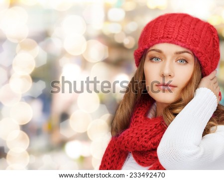 happiness, winter holidays, christmas and people concept - young woman in red hat and scarf over lights background