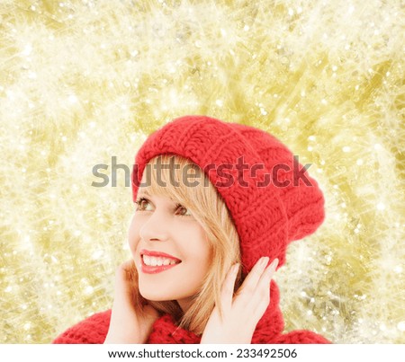 happiness, winter holidays, christmas and people concept - smiling young woman in red hat and scarf over yellow lights background