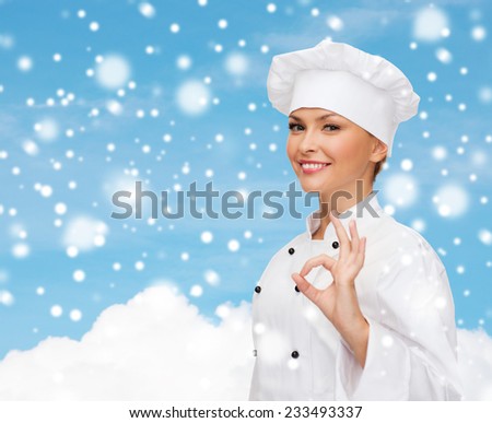christmas, cooking, profession, gesture and people concept - smiling female chef showing ok hand sign over blue snowy sky and cloud background