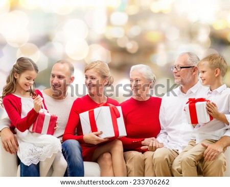 family, holidays, generation, christmas and people concept - smiling family with gift boxes sitting on couch over lights background