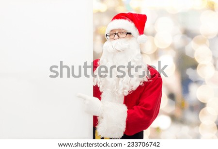 christmas, holidays, advertisement, gesture and people concept - man in costume of santa claus pointing finger to white blank billboard over lights background
