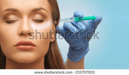 medicine, plastic surgery, beauty, health and people concept - close up of hand in medical glove with syringe making injection to beautiful woman face over blue background