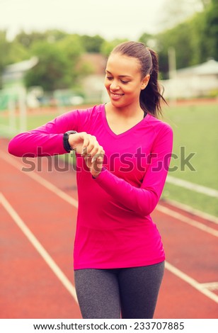 sport, fitness, technology, healthcare and people concept - smiling young woman with heart rate watch on track outdoors