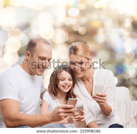 family, holidays, technology and people concept - smiling mother, father and little girl with smartphones over lights background