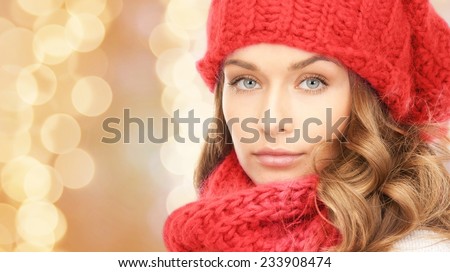 happiness, winter holidays, christmas and people concept - close up of young woman in red hat and scarf over beige lights background