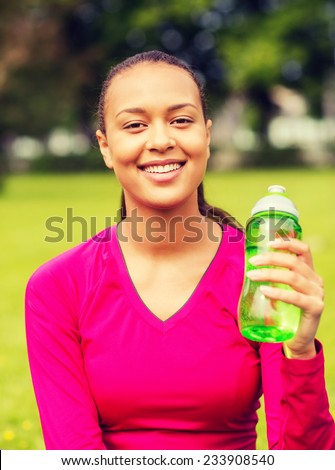 fitness, park, drink and sport concept - smiling african american woman sitting and holding bottle outdoors