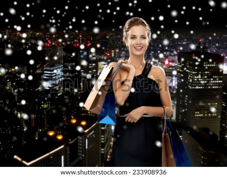 shopping, sale, gifts and holidays concept - smiling woman in dress with shopping bags over snowy night city background