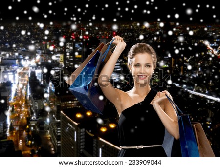 shopping, sale, gifts and holidays concept - smiling woman in dress with shopping bags over snowy night city background