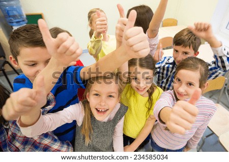 education, elementary school, learning, gesture and people concept - group of school kids and showing thumbs up in classroom