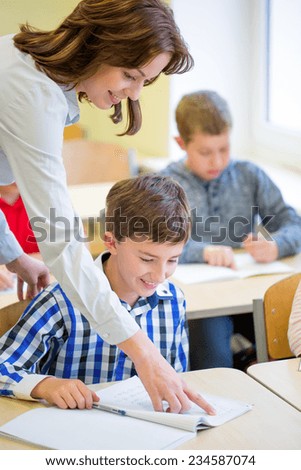education, elementary school, learning and people concept - teacher helping school boy writing test in classroom