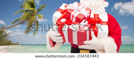 christmas, holidays, travel and people concept - close up of santa claus with gift boxes over tropical beach background