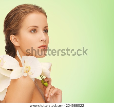 beauty, people and health concept - beautiful young woman with orchid flowers and bare shoulders over green background
