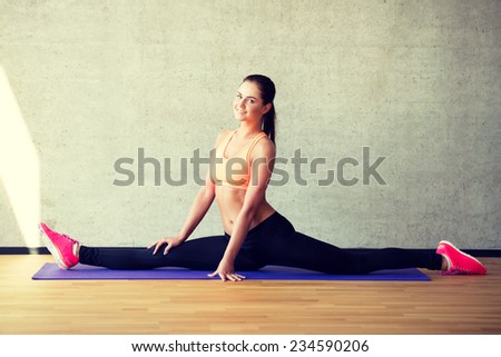 fitness, sport, training and lifestyle concept - smiling woman stretching leg on mat in gym
