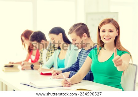 education and school concept - smiling students with textbooks and books and girl in front showing thumbs up at school
